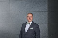 Pekka Leviäkangas seisoo harmaan laatan edessä ja hymyilee. Hänellä on yllään puku ja rusetti.