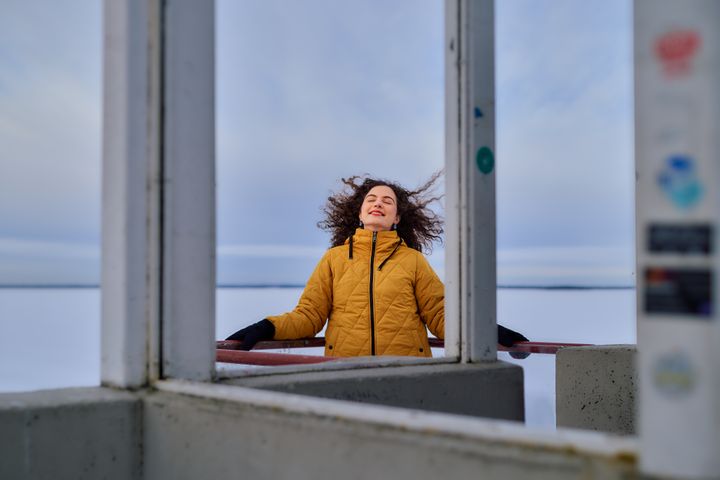 Henkilö nauttii talvisesta säästä jäätyneen veden äärellä, pukeutuneena keltaiseen takkiin.
