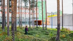 Henkilö kävelee metsän läpi, taustalla näkyy moderni rakennus.