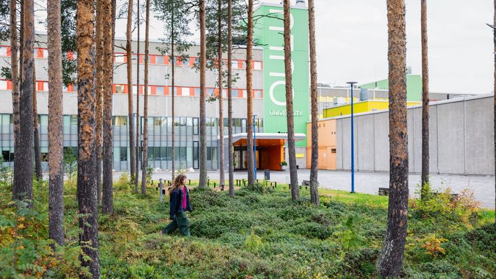 Henkilö kävelee metsän läpi, taustalla näkyy moderni rakennus.