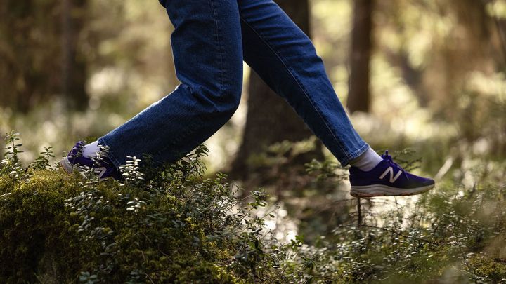 Henkilö kävelee metsäisessä ympäristössä sammaleen peittämällä maalla.