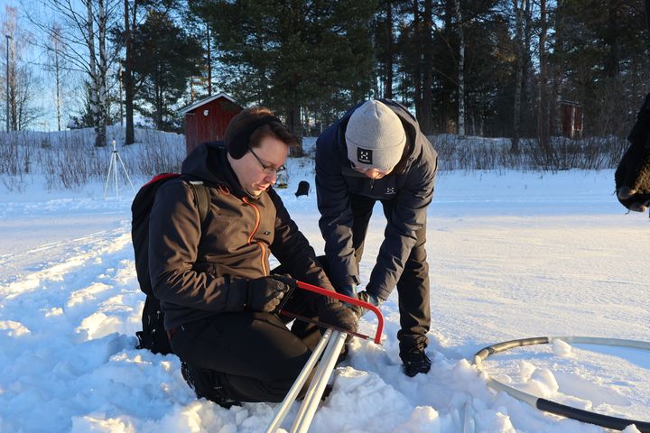Kaksi henkilöä lumessa tekemässä esivalmisteluita tutkimuslaitteen asennusta varten.