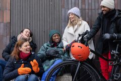 Ryhmä ihmisiä nauraa ja keskustelee talvivaatteissa polkupyörän vieressä.