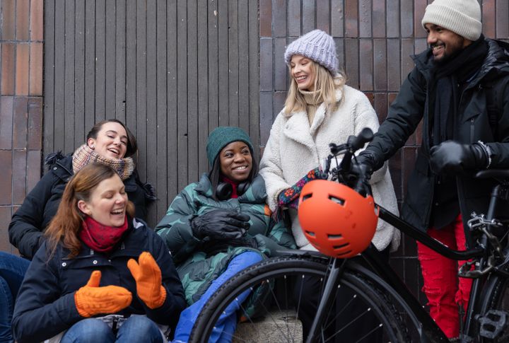 Ryhmä ihmisiä nauraa ja keskustelee talvivaatteissa polkupyörän vieressä.