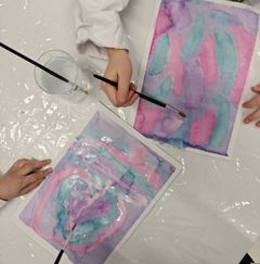 Kaksi henkilöä maalaa vesiväreillä abstrakteja kuvia.