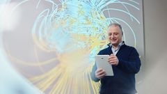 Ilya Usoskin katsoo tablet-laitetta taustallaan maapallon magneettikentän simulaatio.