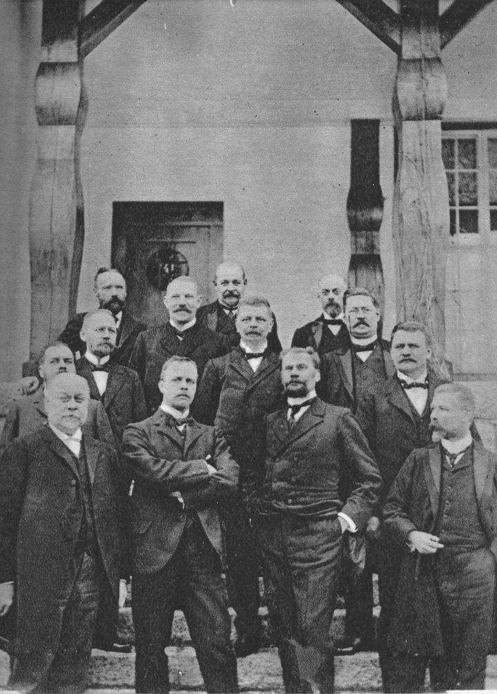 Historiallinen ryhmäkuva miehistä Träskändan kartanon edustalla Espoossa vuonna 1903: Takana P. E. Svinhufvud oven edessä ja Eero Erkko toisena oikealla, edessä Ernst Estlander kädet puuskassa ja Theodor Homén kädet taskuissa.