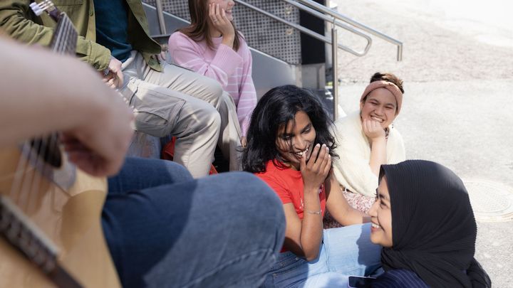 Nuoret istuvat portailla, yksi henkilö soittaa kitaraa. Useilla on iloiset ilmeet.