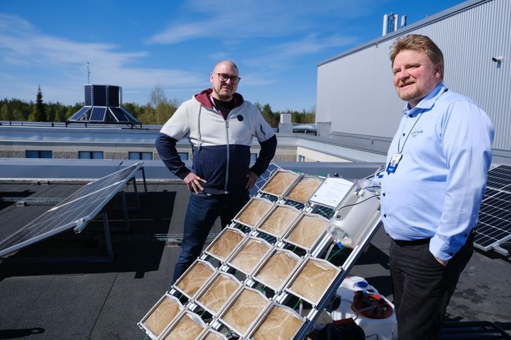 Kaksi miestä seisoo aurinkovetypaneelien vieressä katolla.