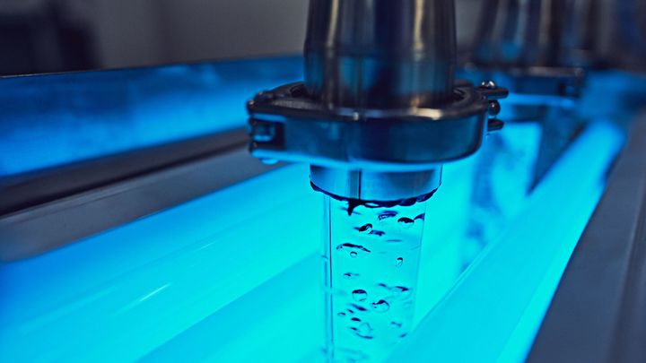 Laboratoriolaitteisto, jossa vettä virtaa putkessa sinisen valon alla.