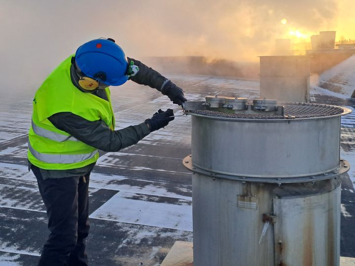 Projektitutkija asentaa näytteenotinta sahakuivaamon katolla.