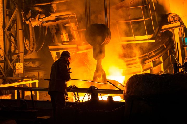 Työntekijä valvoo hehkuvan sulan metallin käsittelyä tehtaassa.