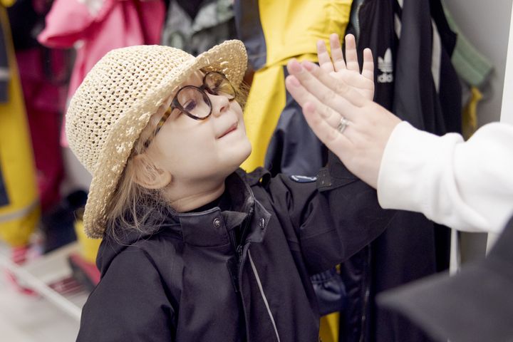 En liten flicka med hatt och glasögon ger en high-five.