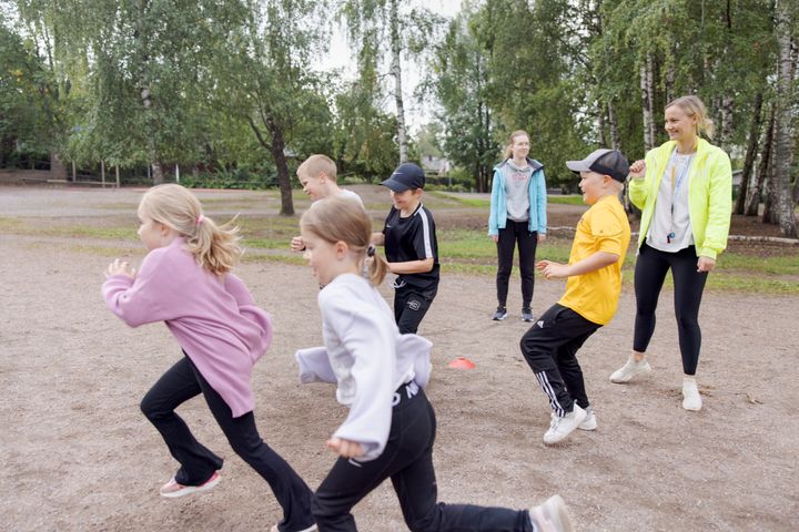 Lapset leikkivät ulkona ohjaajan kanssa.