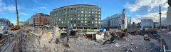 Työmaan laajakulmakuva, jossa purettua lippuhallirakennusta työkoneita ja monttu. Taustalla Kampin useita rakennuksia.