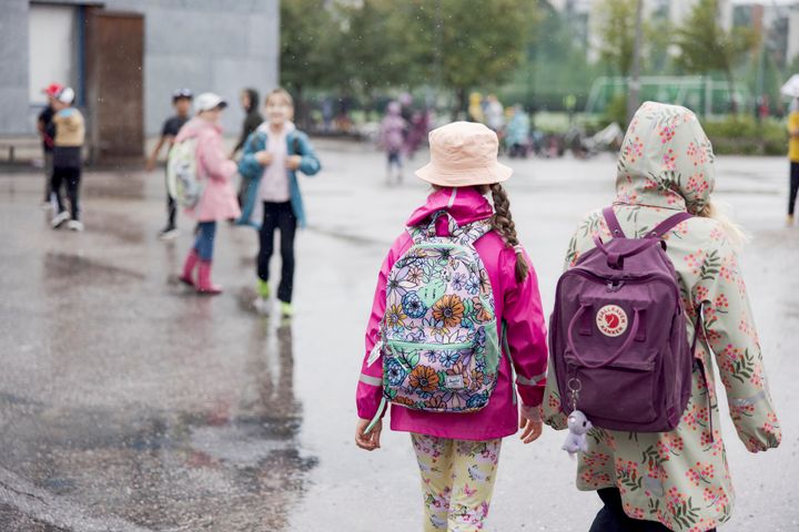 Kaksi lasta kävelemässä koulun pihalla sateisena päivänä.