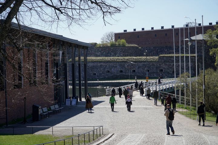 People walking on a pathway near a historic brick building and stone walls.