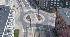 Kuvassa etualalla ylityspaikka, jossa jalankulkijoiden ja pyöräilijöiden on väistettävä raitiovaunua. Ylityspaikan tunnistaa asfalttiin maalatusta raitiovaunun kuvasta ja suojatienmerkkien puuttumisesta keskisaarekkeilta. Liikenneympyrän takana normaali suojatie.