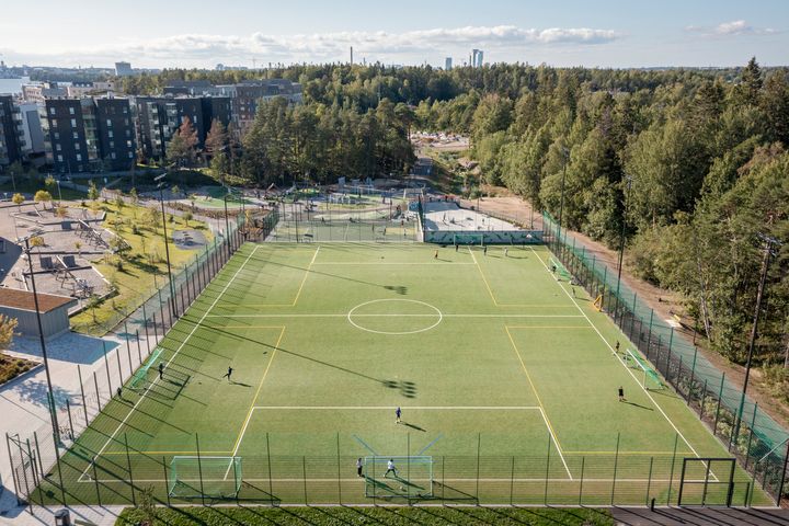 Ilmakuva jalkapallon tekonurmikentältä, ympärillä metsää ja rakennuksia.