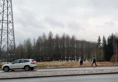 Tiellä kulkee auto ja sen vieressä on voimajohto. Taustalla kasvaa puita.