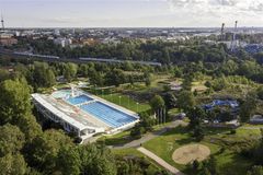 På bilden ses en simbassäng med blått vatten omgärdat av grönområden. Bilden är lockande och somrig.