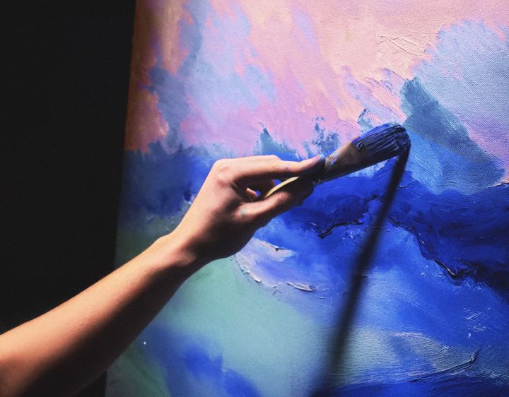 Henkilön käsi maalaa sinisävyistä taulua.