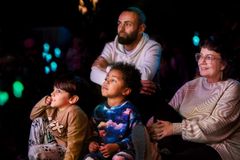 Kaksi lasta ja kaksi aikuista seuraa esitystä salissa, jonka valot on himmennetty.