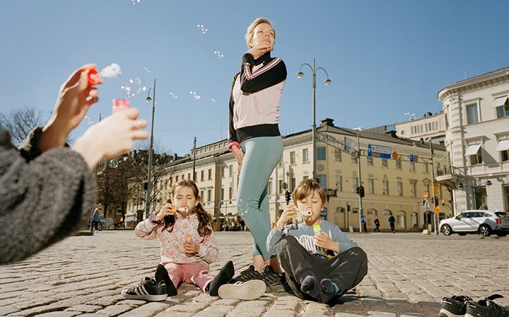Nainen poseeraa, etualalla kaksi lasta puhaltaa saippukuplia.