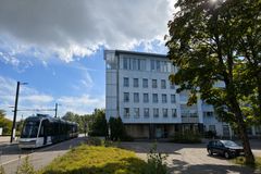 Spårvagn och buss stannar nära en modern byggnad omgiven av träd.