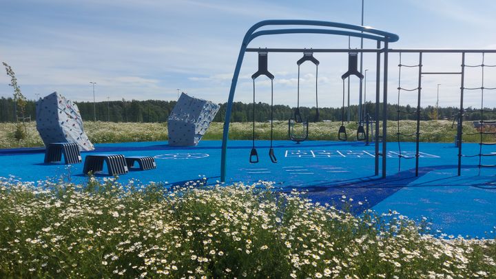 Kiipeilytelineitä puistossa sinisellä alustalla.