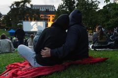 Kaksi ihmistä istuu nurmikolla selin katsomassa ulkoilmaelokuvaa.