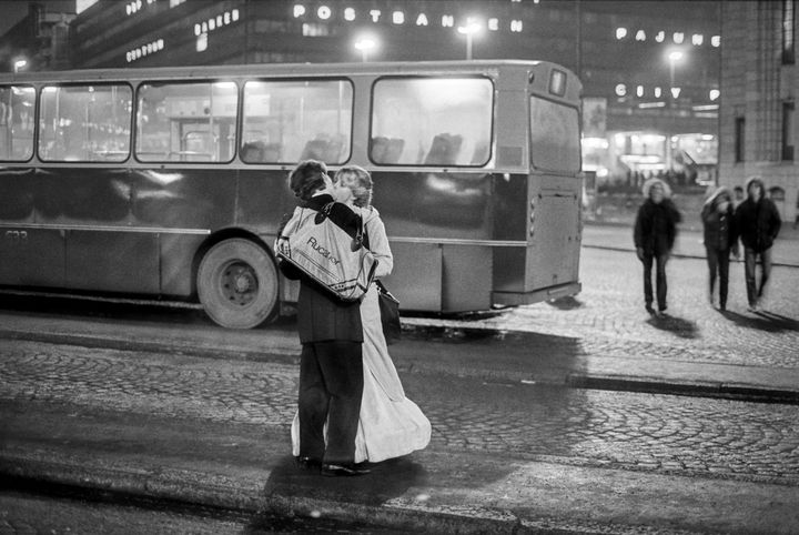 En svartvit bild av ett par som dansar framför en äldre buss på en stadsgata.