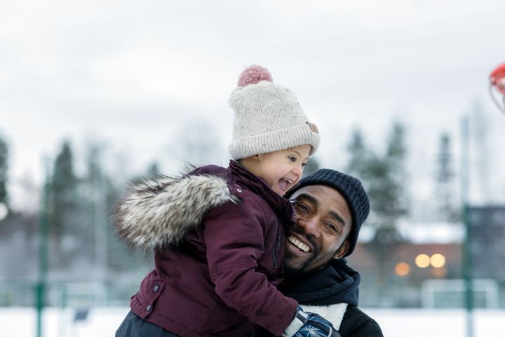 En leende vuxen och ett barn i vinterkläder leker utomhus.