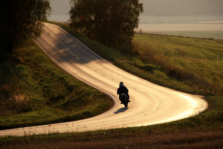 Moottoripyöräilijä ajaa yksin maaseudun mutkaista tietä.