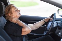 Iäkäs nainen ajaa autoa niskaa pidellen.