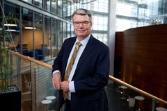 Kuvassa on asiantuntija seisomassa modernissa toimistorakennuksessa. Hänellä on päällään tumma puku.