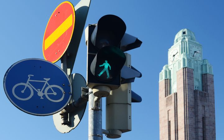 Liikennevalot, pyöräily- ja jalankulkukyltti. Taustalla näkyy torni.