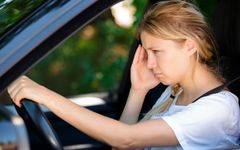 Nuori nainen ajaa autoa ja näyttää väsymyneeltä tai stressaantuneelta.