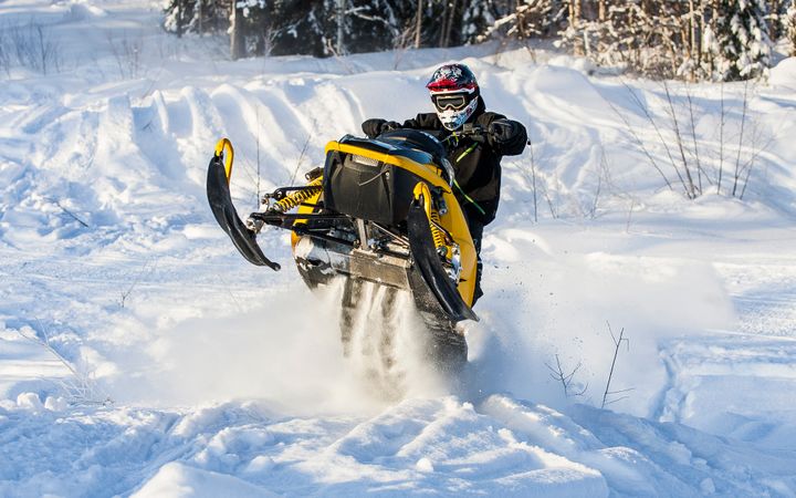 Moottorikelkka nousee vauhdilla lumeen peitetyllä maastolla. Kuljettaja käyttää kypärää ja suojalaseja.