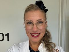 Lääkäri katsoo kameraan hymyillen lääkärintakki päällä.