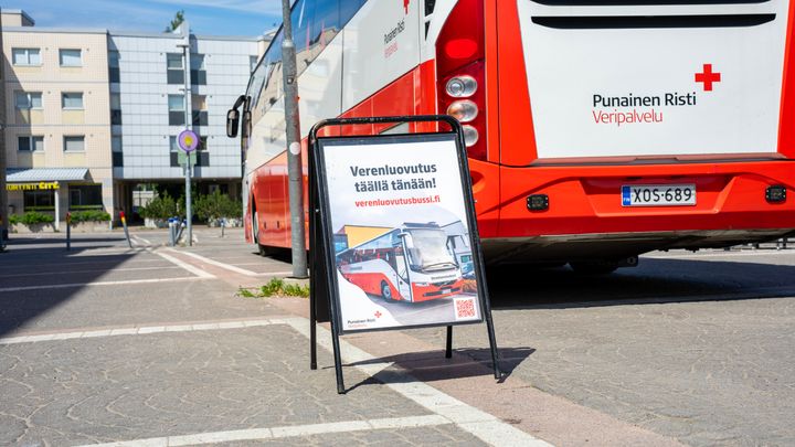 Verenluovutusbussi pysähtyneenä toriaukiolle. Bussin edessä on kyltti, jossa lukee: Verenluovutus täällä tänään!