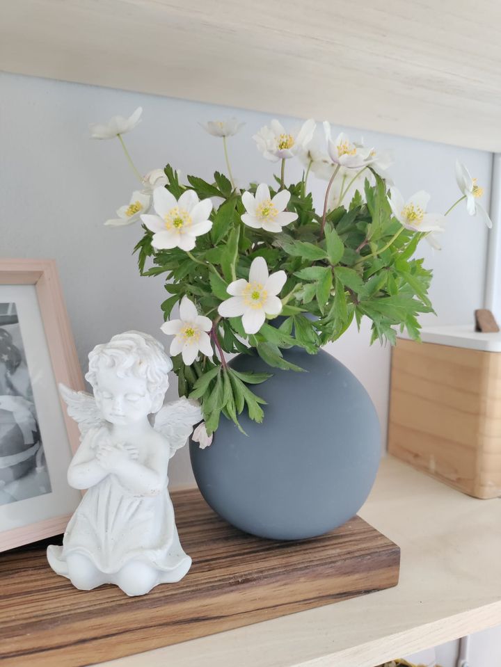 Hyllyllä enkelipatsas, kukkia ja kuolleen lapsen kuva osittain näkyvissä