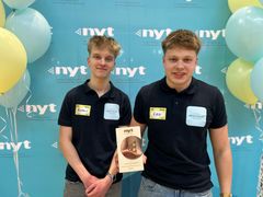 Kaksi nuorta seisoo kuvausseinäkkeen edessä Uskalla Yrittää -palkinnnon kanssa.