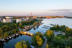 Ilmakuva kaupungista meren rannalla, jossa näkyy puistoalueita, venesatama ja rakennuksia auringonlaskun valossa.