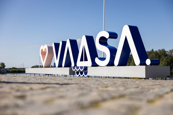 Kyseessä on iso nimikyltti, jossa lukee "Vaasa" ja sitä edeltää sydänsymboli. Tausta on aurinkoinen ja kirkas.