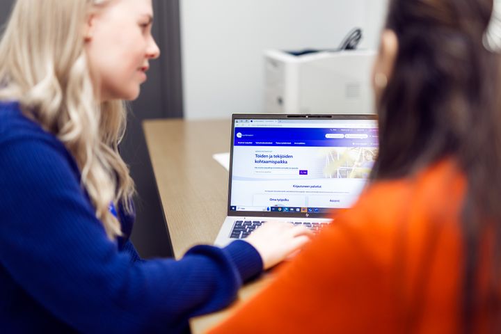Två personer sitter vid ett bord framför en bärbar dator och tittar på skärmen.