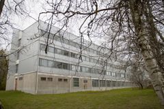Kolmikerroksinen harmaa rakennus lehtipuiden lomassa.