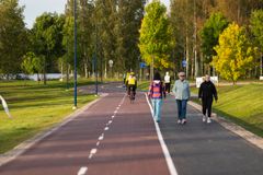En cykel- och gångväg med flera personer som promenerar och en person som cyklar, omgiven av träd och grön gräsmatta.