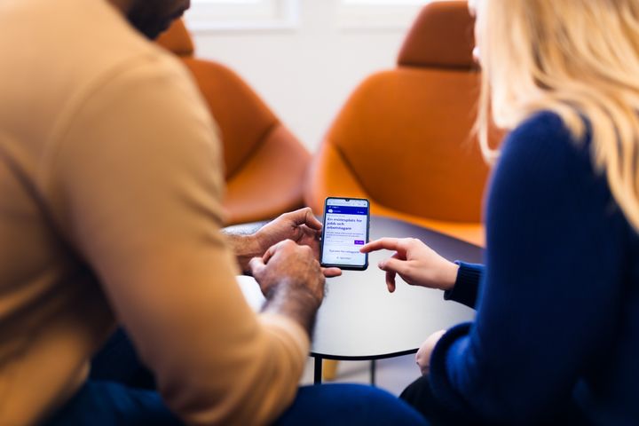 Två personer sitter tillsammans och tittar på en mobiltelefon.