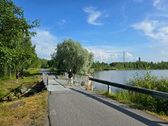 Personer som promenerar på en bro som går över vattnet. I bakgrunden finns en park och havet.